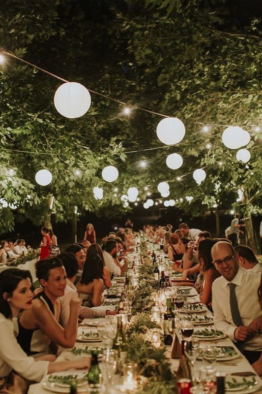 Mesa larga de banquete bajo farolillos y globos de luz
