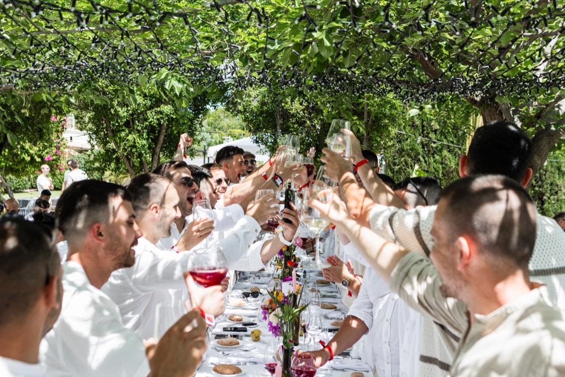 Invitados brindando en una mesa larga bajo los árboles
