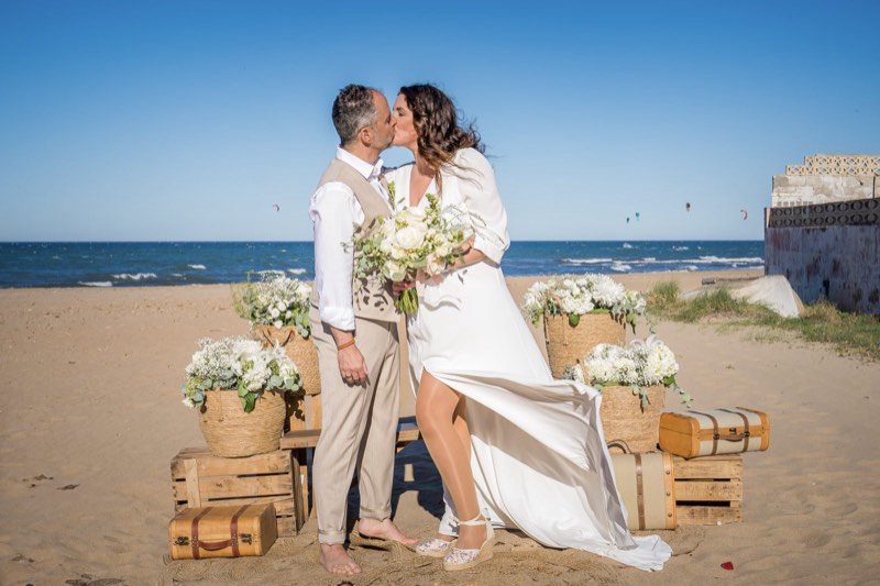 Los novios en la ceremonia en la playa, entre cajas de madera y flores