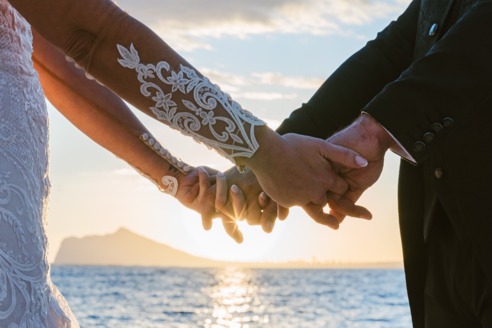 Manos entrelazadas de los novios con el mar al fondo